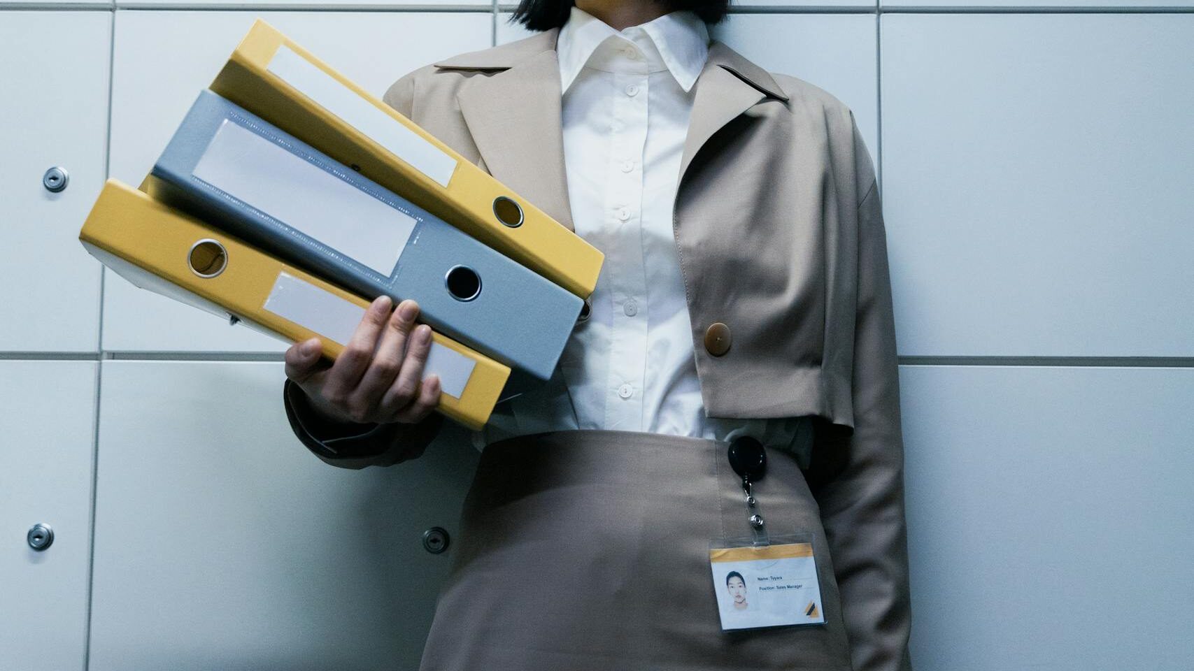 Businesswoman in formal attire holding binders in an office environment, showcasing professionalism.